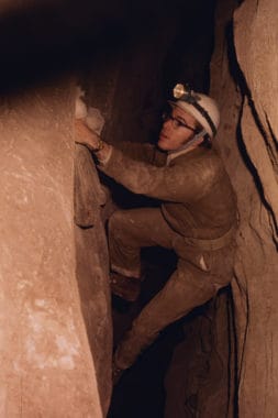 Merlin Tuttle climbing high above floor in Fern Cave, Alabama to reach banded gray myotis in 1970. The bags contain banded bats.